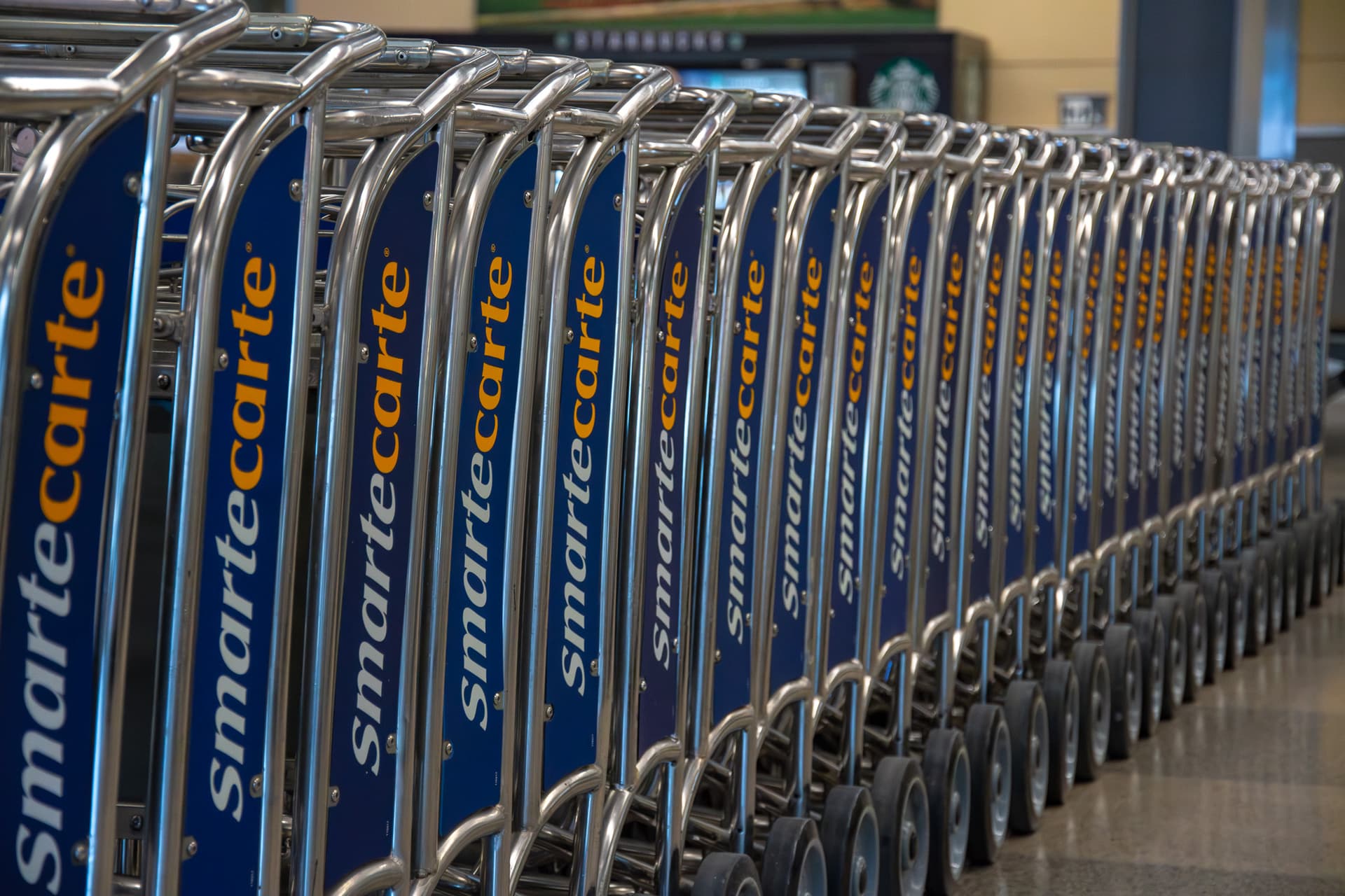 Row of blue and silver shopping carts with Smartecarte branding lined up in an airport terminal.