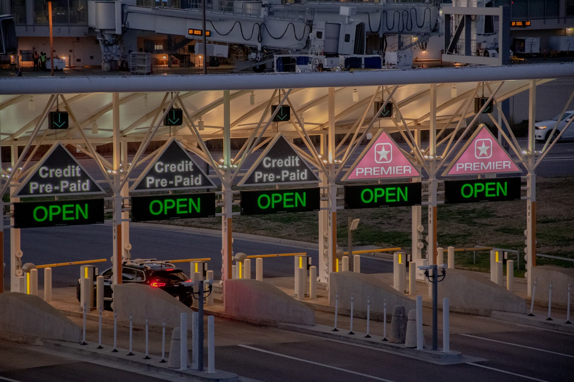 Parking entrance plaza with multiple lanes showing illuminated green OPEN signs, Credit Pre-Paid and Premier lanes, with a car passing through.