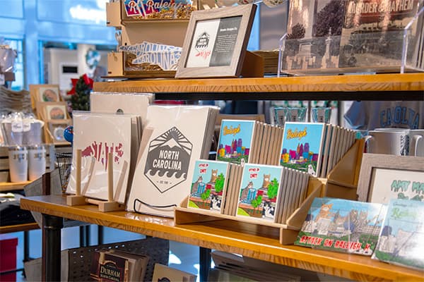Wooden shelves displaying various greeting cards and postcards, including North Carolina themed items and colorful illustrated designs.