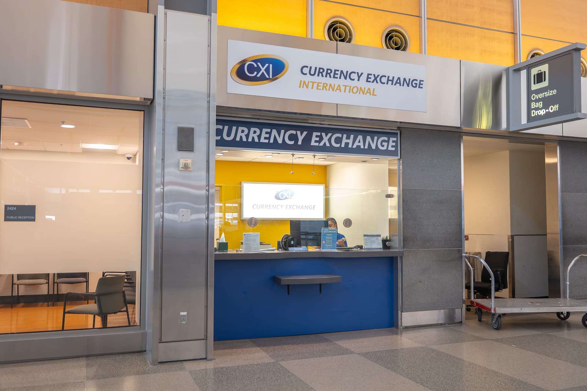 CXI Currency Exchange International kiosk in an airport with blue counter, yellow interior walls and service window.