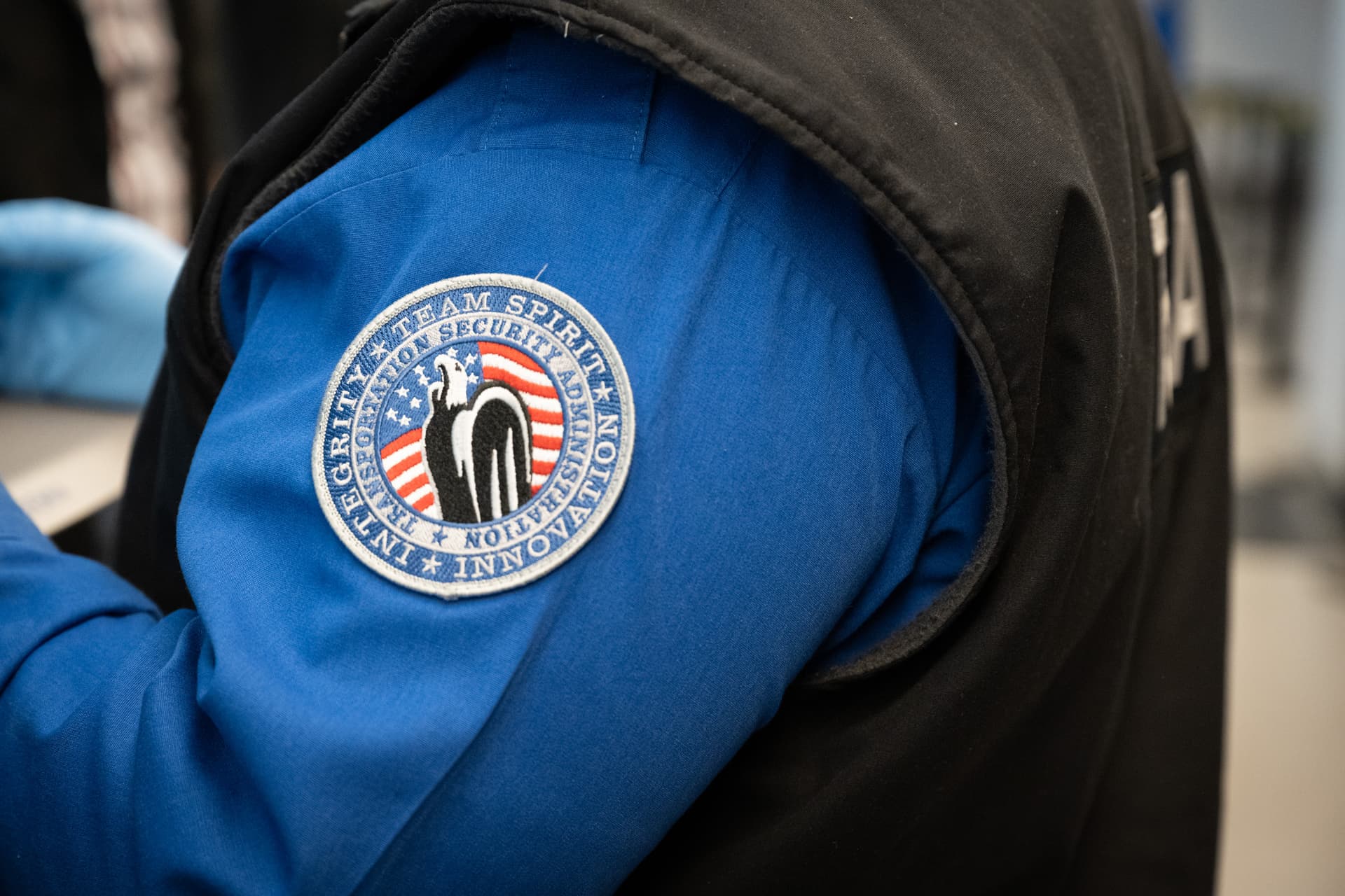 Close-up of TSA officer's blue uniform shirt with circular Transportation Security Administration patch featuring American flag