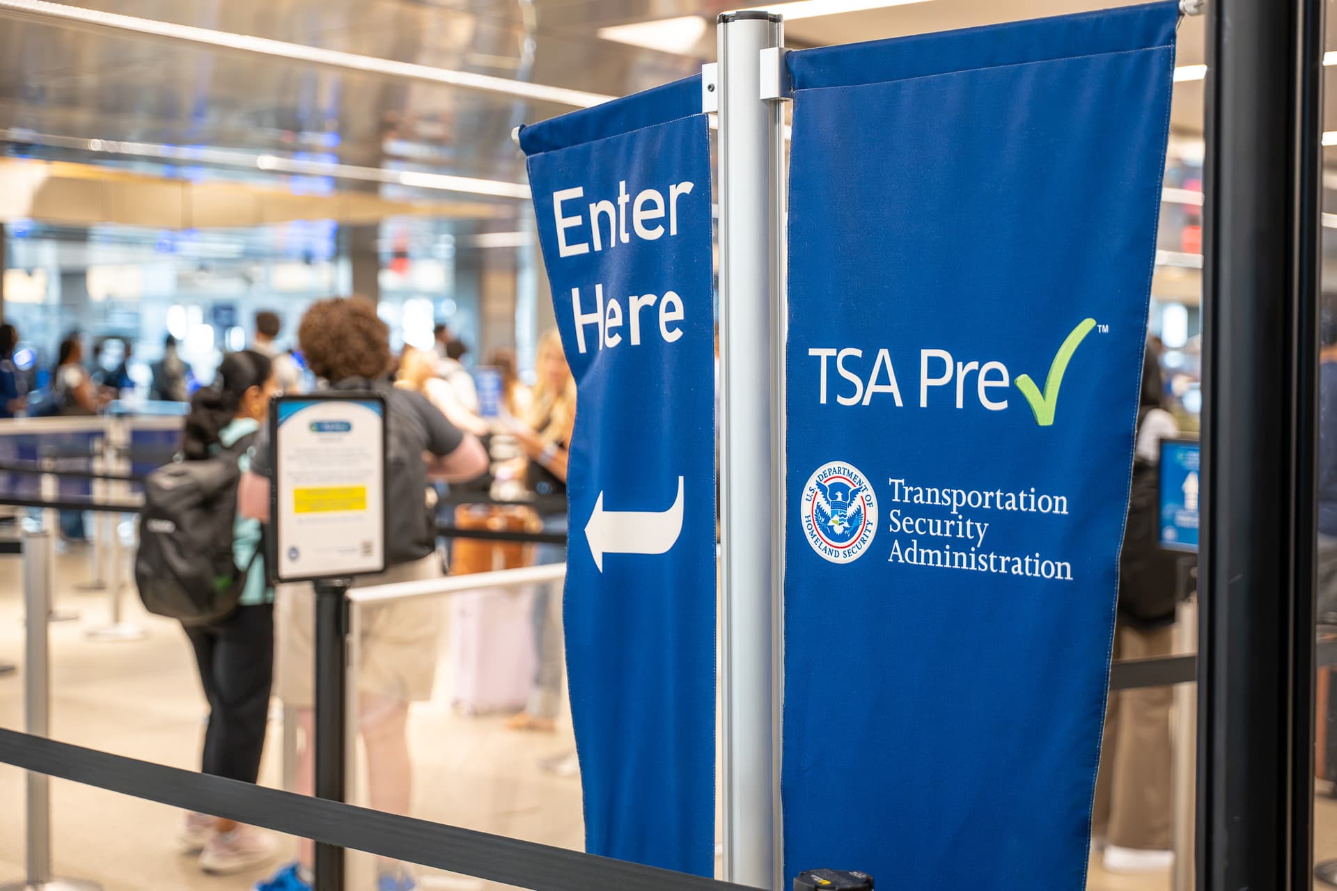 Blue TSA PreCheck sign with white text and arrow directing travelers to expedited security screening entrance at airport.