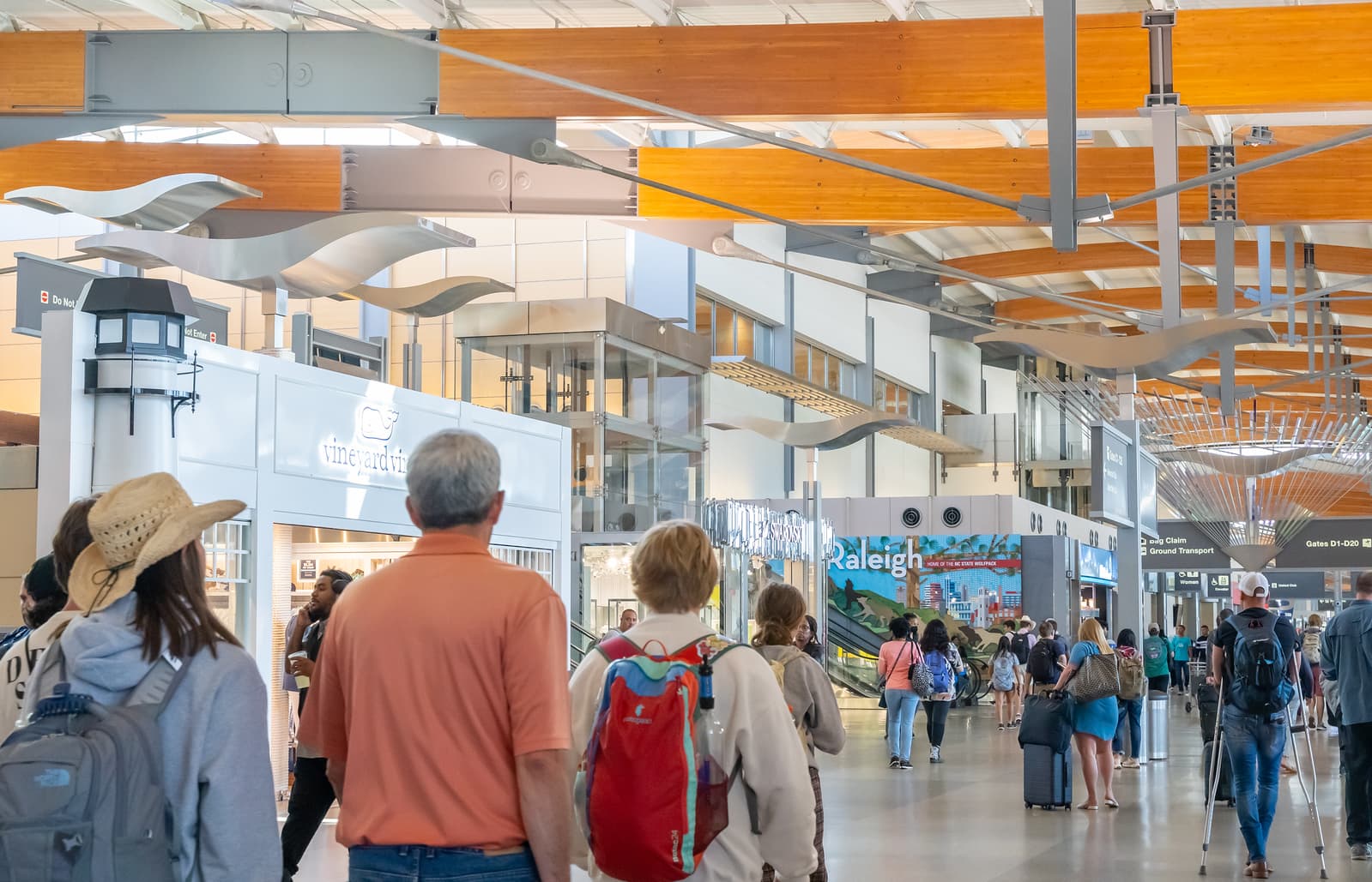 Travelers walking through Raleigh-Durham International Airport Terminal 2 with wooden ceiling beams and white sculptural elements overhead.