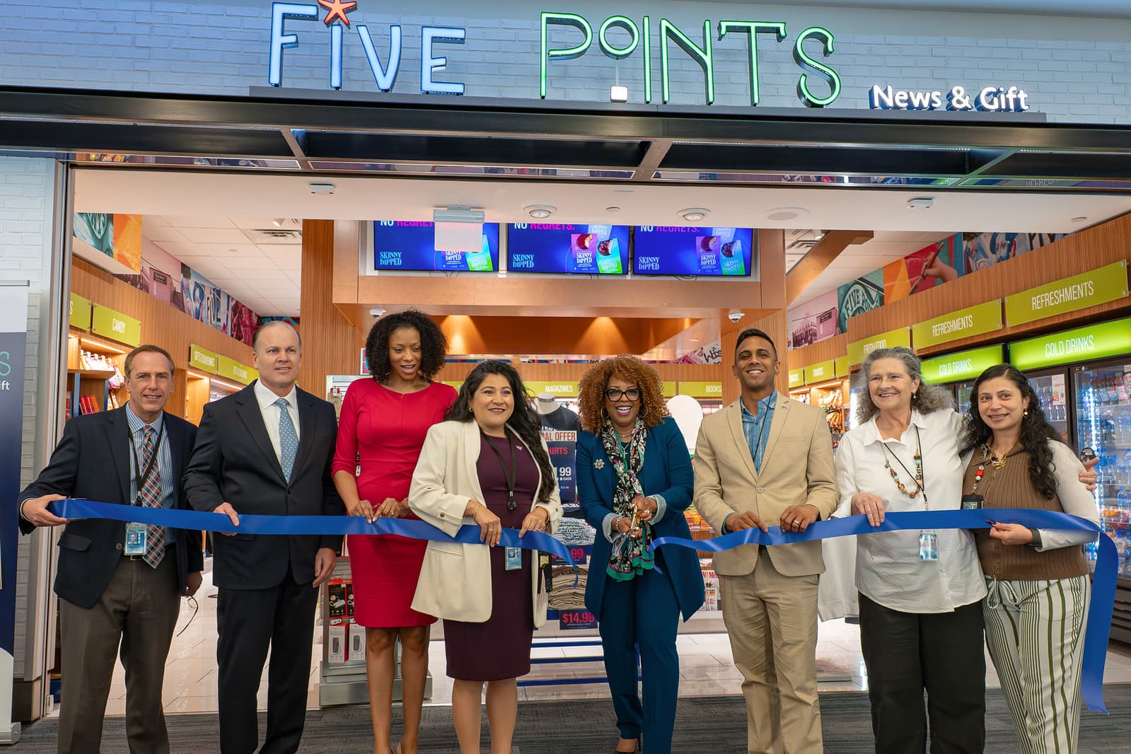 RDU Board, executives and business managers holding blue ribbon at Five Points News & Gift store grand opening ceremony